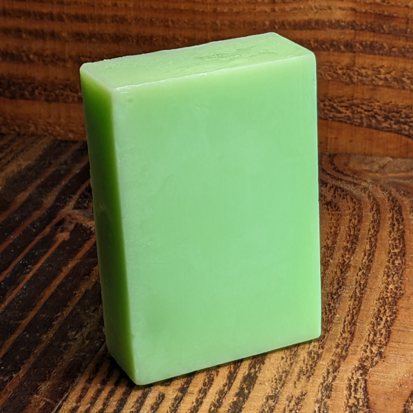 A solid green glycerin soap bar resting on a wooden background, infused with the essence of tea tree and eucalyptus oils.