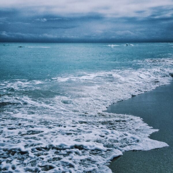 Gentle ocean waves rolling onto the shore under a cloudy sky, representing the refreshing Sea Breeze fragrance